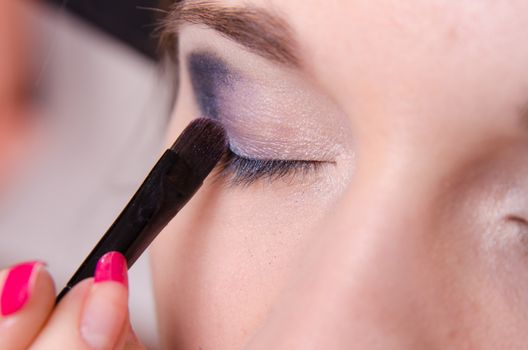 Makeup artist paints the eyelids of a beautiful young girl in the makeup