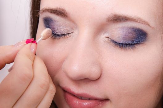Makeup artist paints the eyelids of a beautiful young girl in the makeup