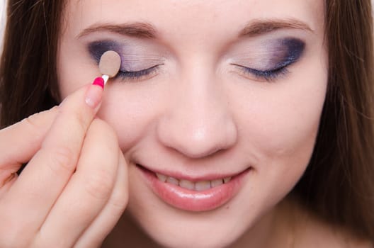 Makeup artist paints the eyelids of a beautiful young girl in the makeup