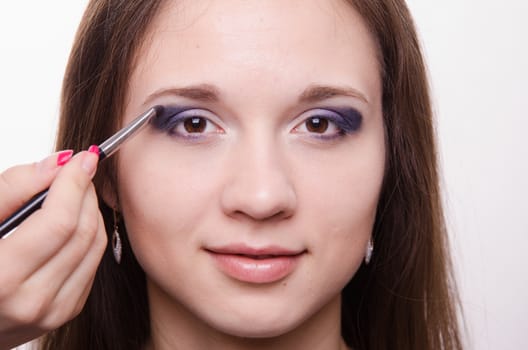 Makeup artist paints the eyelids of a beautiful young girl in the makeup