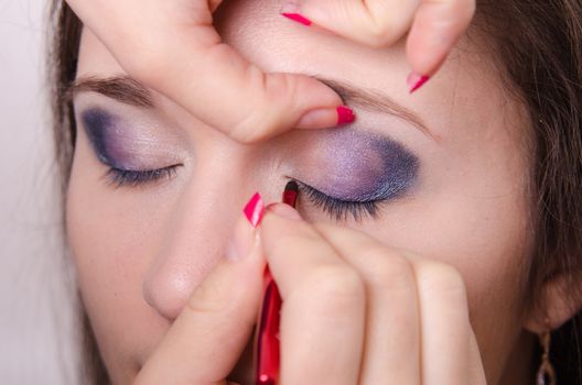 Makeup artist paints eyelashes of a beautiful young girl in the makeup