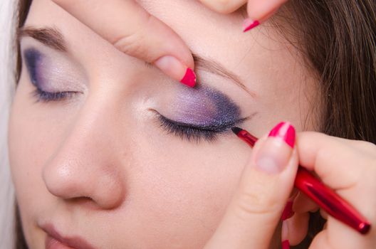 Makeup artist draws arrows beautiful young girl in the makeup