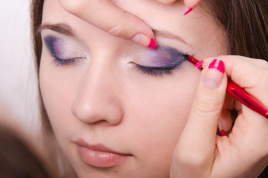 Makeup artist draws arrows beautiful young girl in the makeup