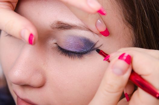 Makeup artist draws arrows beautiful young girl in the makeup