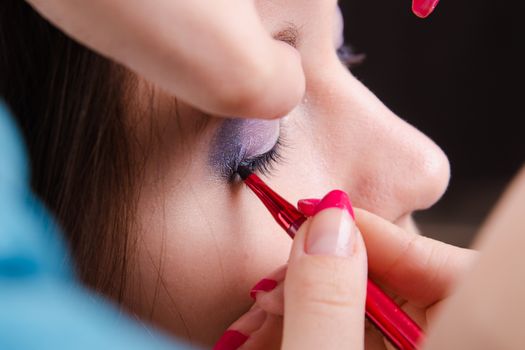 Makeup artist draws arrows beautiful young girl in the makeup