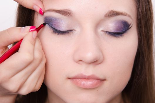 Makeup artist draws arrows beautiful young girl in the makeup