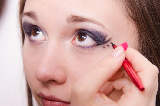 Makeup artist draws arrows beautiful young girl in the makeup