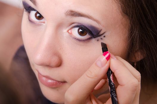 Makeup artist draws arrows beautiful young girl in the makeup