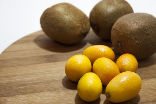 Kumquat and kiwi on the wooden board.