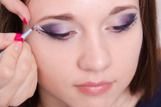 Makeup artist draws arrows beautiful young girl in the makeup