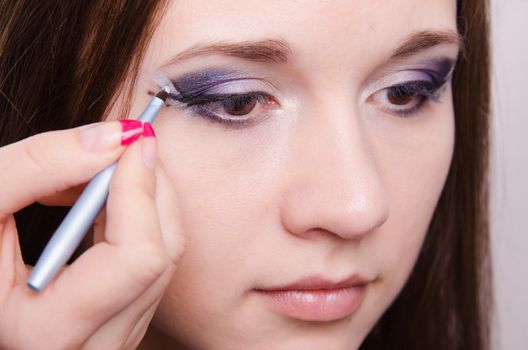 Makeup artist draws arrows beautiful young girl in the makeup