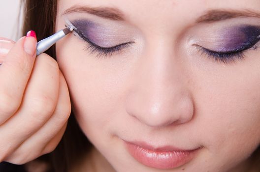 Makeup artist draws arrows beautiful young girl in the makeup