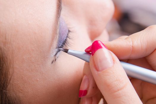 Makeup artist draws arrows beautiful young girl in the makeup