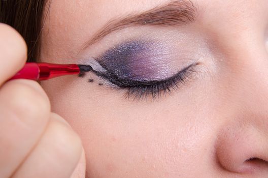 Makeup artist draws arrows beautiful young girl in the makeup