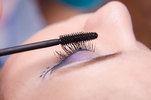 Makeup artist paints eyelashes of a beautiful young girl in the makeup