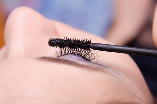 Makeup artist paints eyelashes of a beautiful young girl in the makeup