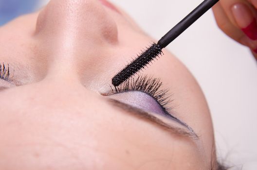Makeup artist paints eyelashes of a beautiful young girl in the makeup