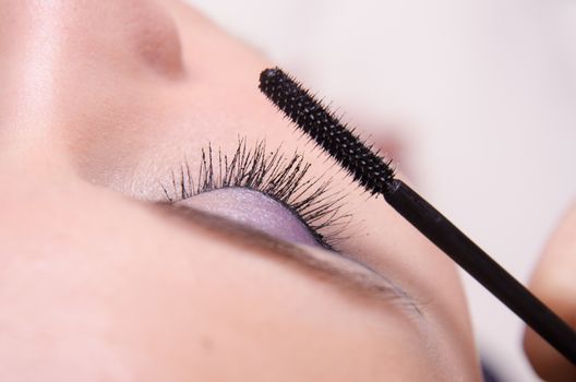 Makeup artist paints eyelashes of a beautiful young girl in the makeup
