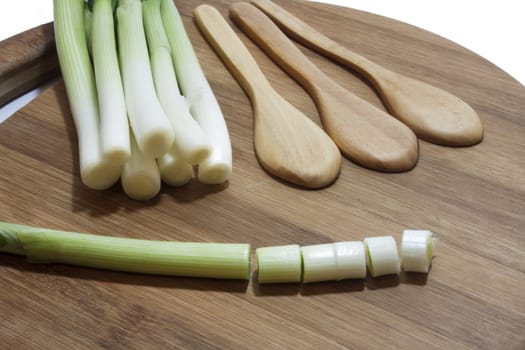Young onions and the wooden spoons on the kitchen wooden board.