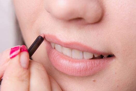 Makeup artist paints her lips a beautiful young girl in the makeup