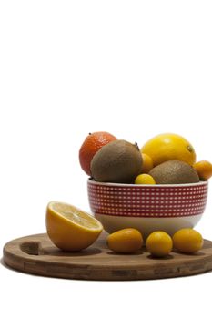 Fruit arrangement in the bowl and on the kitchen wooden board. Lemon, kumquat, kiwi and tangerine in the bowl and on the kitchen wooden board.