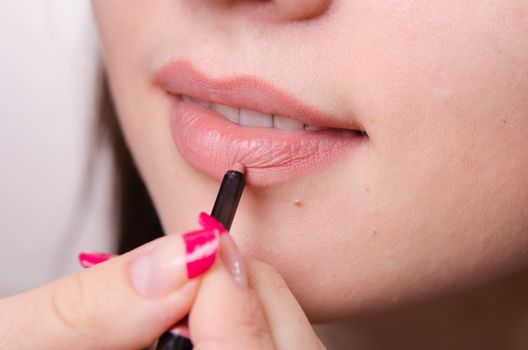 Makeup artist paints her lips a beautiful young girl in the makeup