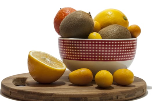 Fruit arrangement in the bowl and on the kitchen wooden board. Lemon, kumquat, kiwi and tangerine in the bowl and on the kitchen wooden board.