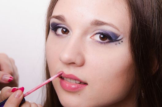 Makeup artist paints her lips a beautiful young girl in the makeup