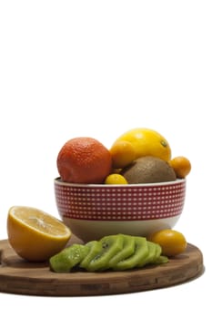 Fruit arrangement in the bowl and on the kitchen wooden board. Lemon, kumquat, kiwi and tangerine in the bowl and on the kitchen wooden board.