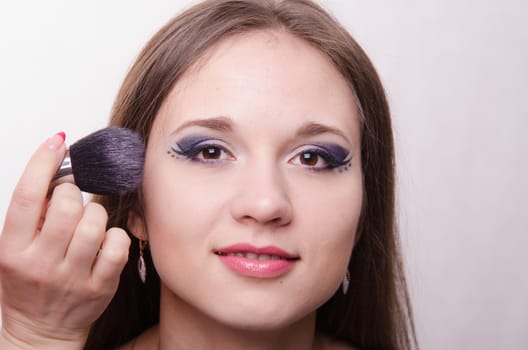 Makeup artist brush powder gets on the face of a beautiful young girl in the makeup