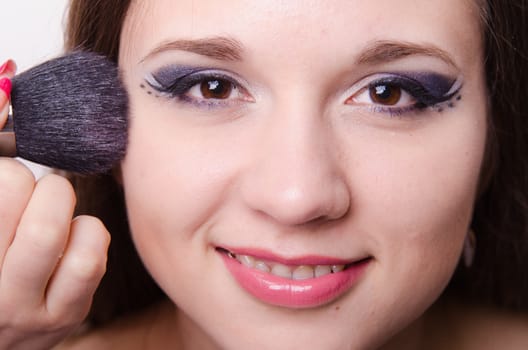 Makeup artist brush powder gets on the face of a beautiful young girl in the makeup