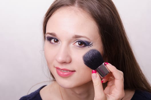 Makeup artist brush powder gets on the face of a beautiful young girl in the makeup