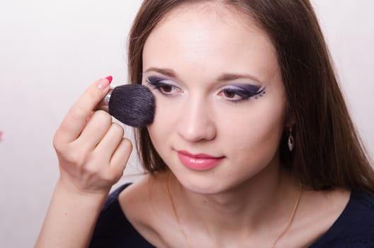 Makeup artist brush powder gets on the face of a beautiful young girl in the makeup