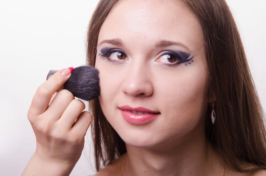 Makeup artist brush powder gets on the face of a beautiful young girl in the makeup