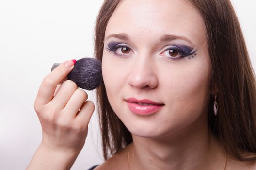 Makeup artist brush powder gets on the face of a beautiful young girl in the makeup