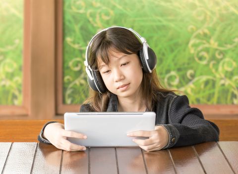 Portrait asian young girl is listening to music through headphones by sitting using Digital Tablet