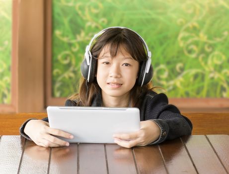 Portrait asian young girl is listening to music through headphones by sitting using Digital Tablet