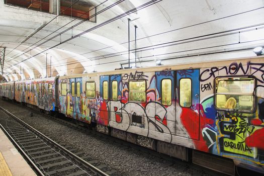 Colorful graffiti on the sides of the carriages an underground tube train parked in a metro station viewed across the track