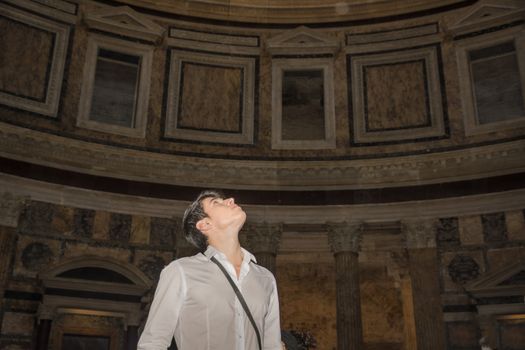 Handsome young tourist in Rome standing looking up into the dome of a historic church in Rome as he admires the architecture and decoration