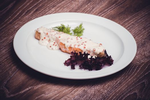 salmon fillet with caviar cream sauce on white plate 