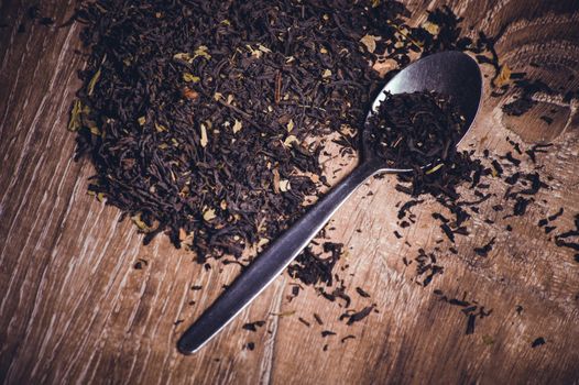 black tea dried leafs on spoon  on wooden background 