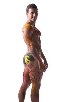 Muscular young man shirtless with skin painted with Holi colors, looking at camera smiling