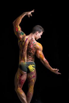 Back of muscular young man shirtless with skin painted with Holi colors, looking down