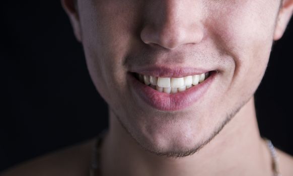 Close up of white teeth and lips of a smiling young man on dark background