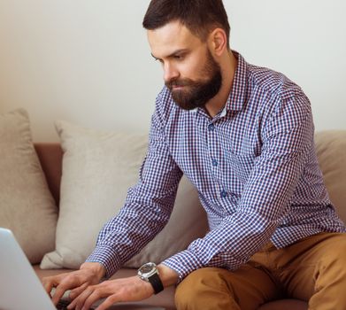 Young bearded man working on laptop at home