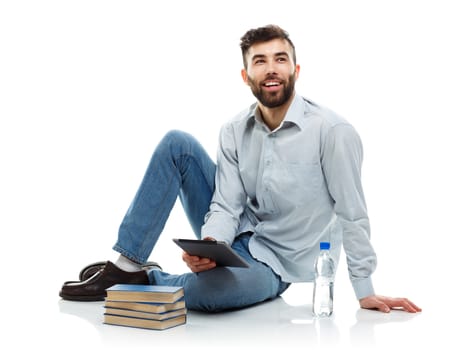 Young bearded smiling man holding a tablet with books and a bottle of water sitting on a white background
