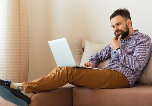 Young bearded man working on laptop at home