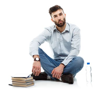 Young bearded smiling man holding a tablet with books and a bottle of water sitting on a white background