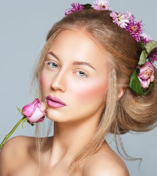 Lovely model with shiny volume curly hair with flowers, winter white eyelashes make-up, vivid lips and pink cheeks. Christmas look