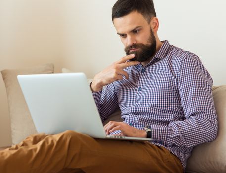 Young bearded man working on laptop at home